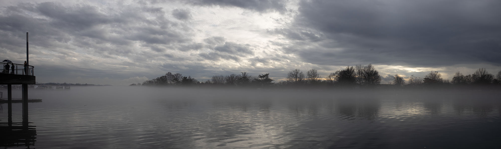 Layer of Fog on a Wintry Body of Water, With Dock to Left and Trees Across.